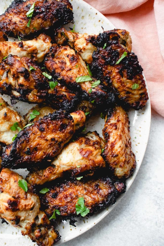 speckled grey plate with balsamic glazed chicken wings garnished with chopped cilantro with a pink cloth napkin in the background