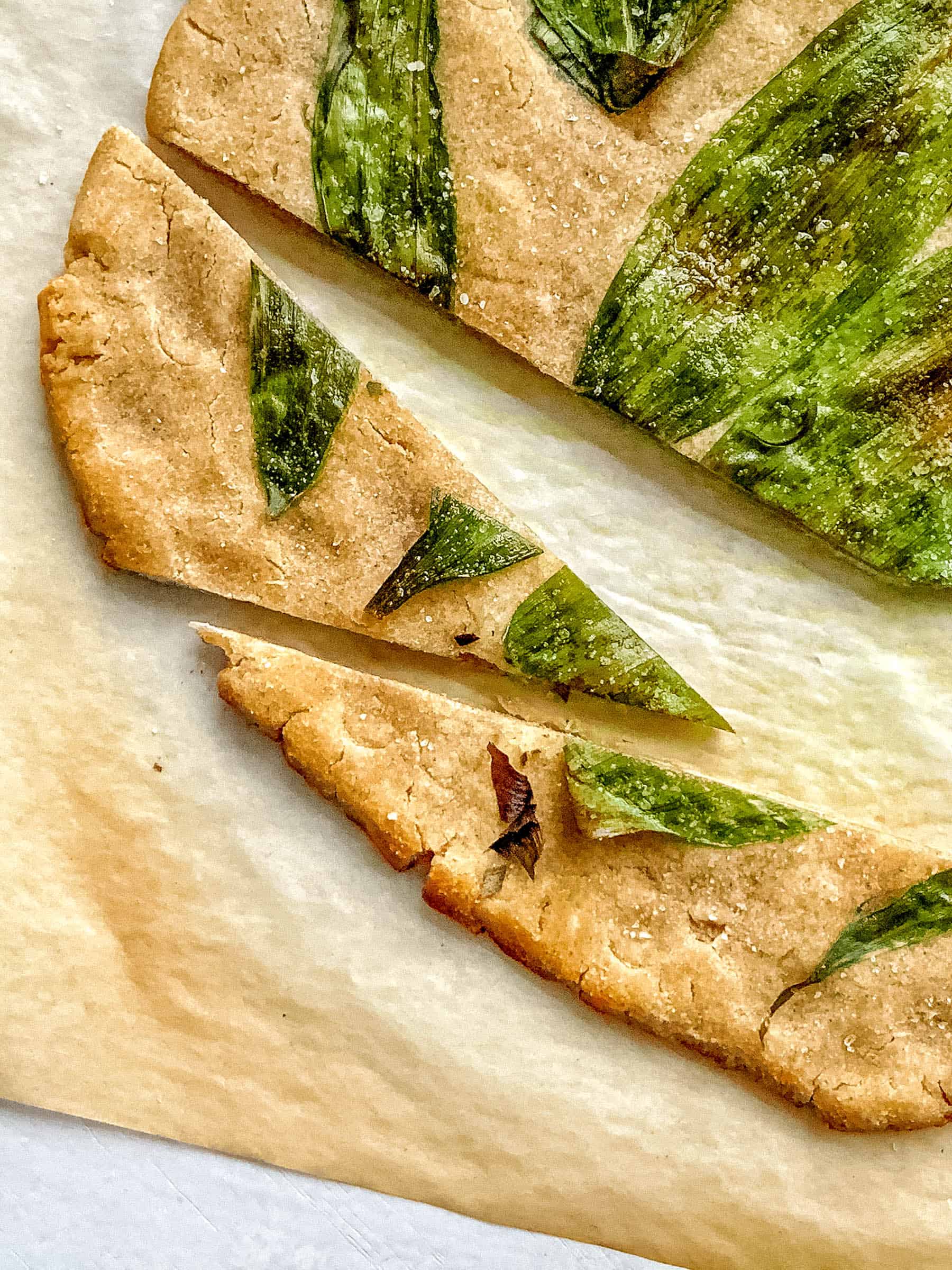 three slices of sourdough flatbread topped with wild leeks on a piece of parchment paper