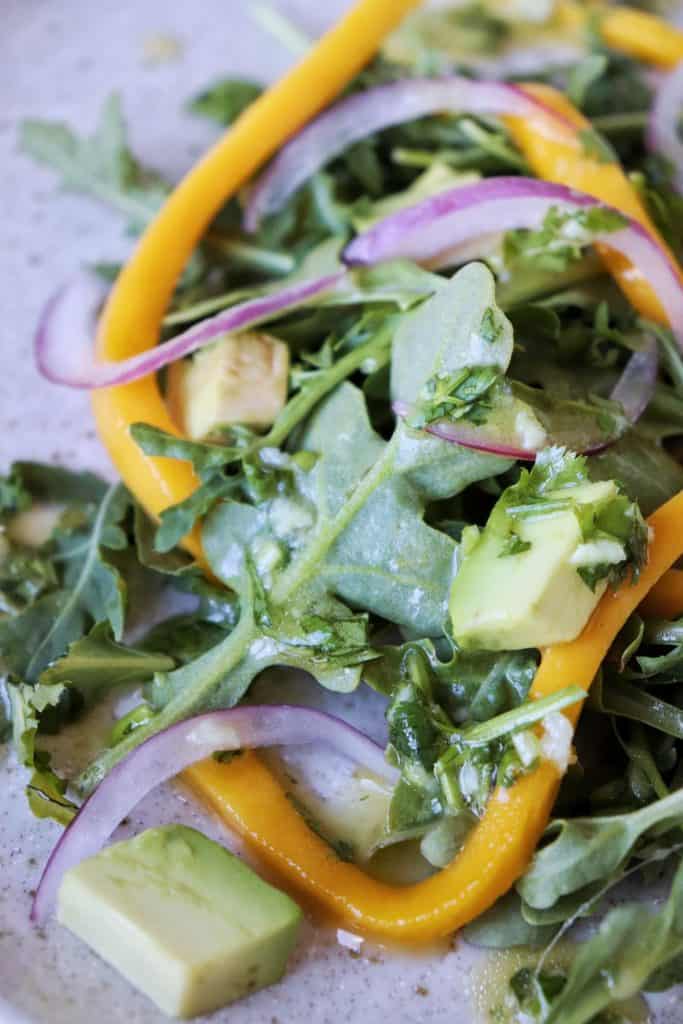 Close up image of Arugula Mango Avocado Salad on light brown speckled plateplate