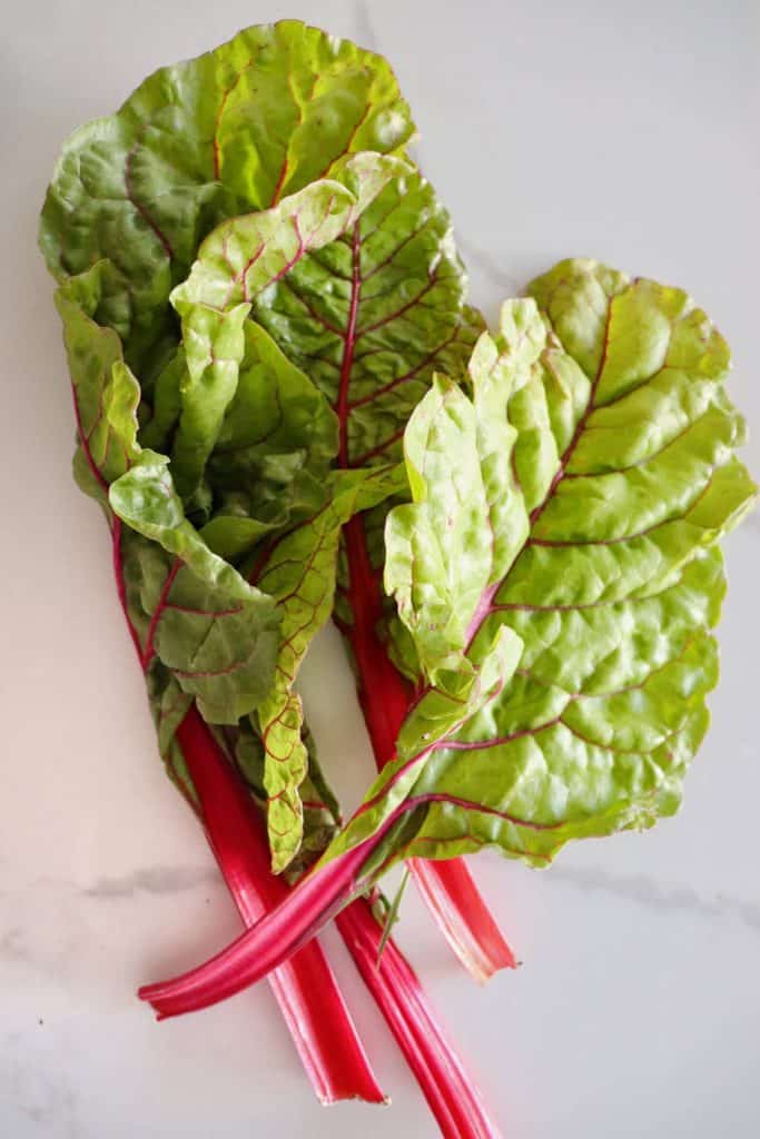 four red steams of swiss chard with green leaves on a white and grey marbled backdrop 
