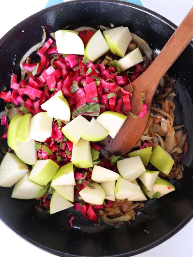black cast iron skillet with chopped red swiss chard stems, and chopped granny smith apples with a light wooden spoon