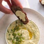 Hand dipping piece of toast into Garlic Scape Hummus (AIP)