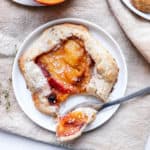 close up shot of peach thyme galette on white plate with fork holding one bite of galette