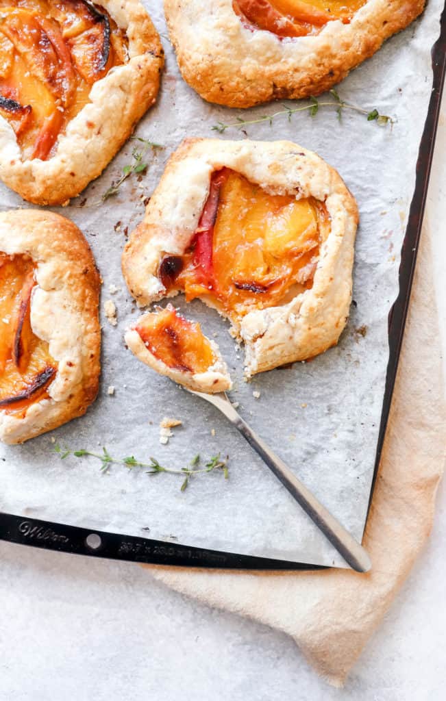 Baking sheet with white parchment paper with four mini peach galettes with a fork 