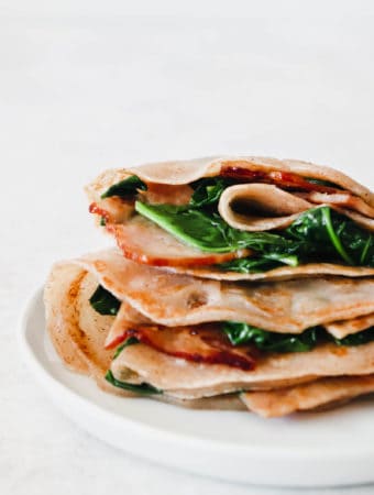 Two AIP Crepes stuffed with bacon and spinach on a white plate
