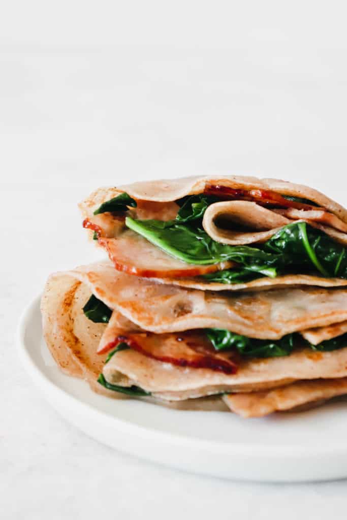 Two AIP Crepes stuffed with bacon and spinach on a white plate