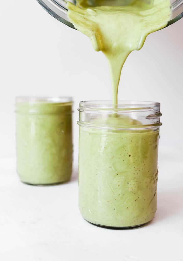 Two glasses of peach green smoothie with blender pouring drink into one of the glasses