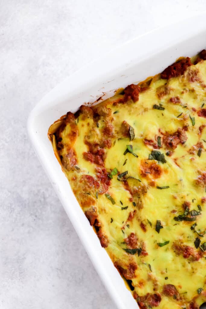 Close up shot of lasagna topped with chopped basil in a white baking dish on a grey backdrop 