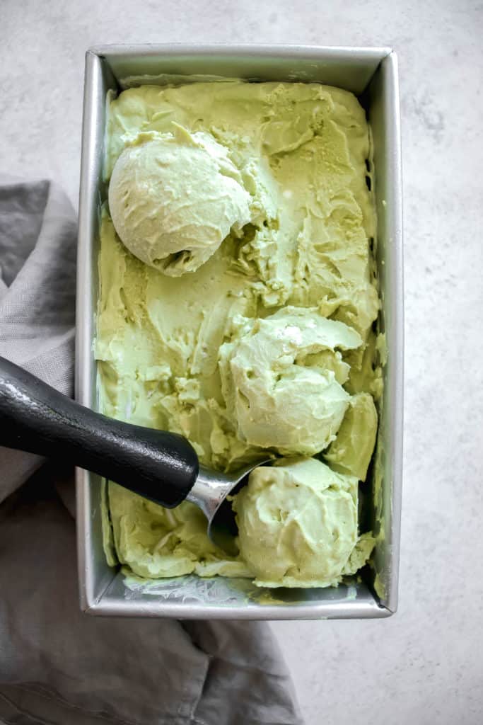 loaf pan with matcha ice cream with three scoops and an ice cream scoop
