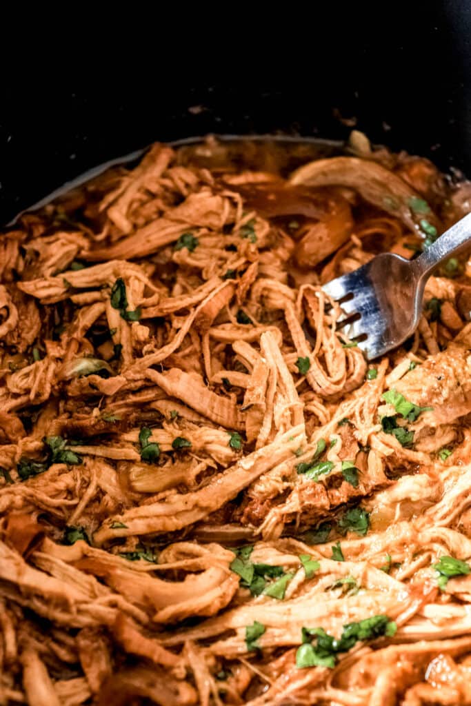 close up shot of pulled pork in a slow cooker with a fork