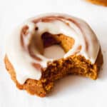 close up shot of pumpkin spice donut with coconut butter frosting on a white background with two donuts in the background