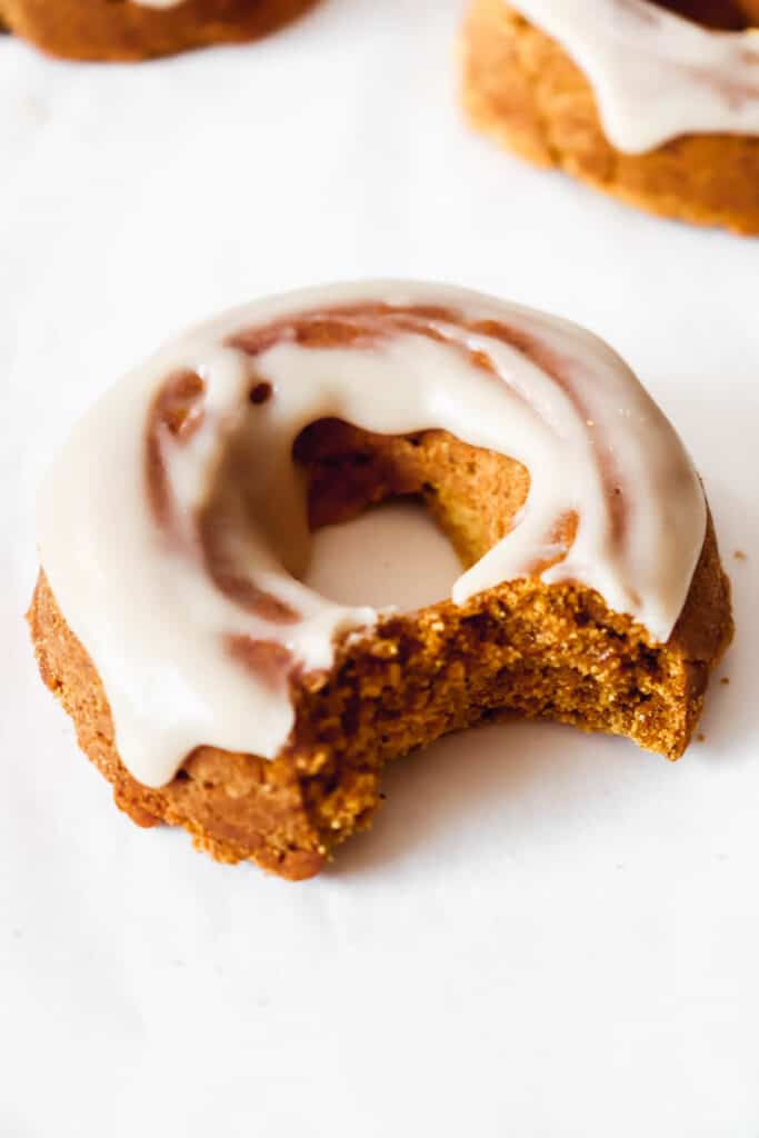 close up shot of pumpkin spice donut with coconut butter frosting on a white background with two donuts in the background