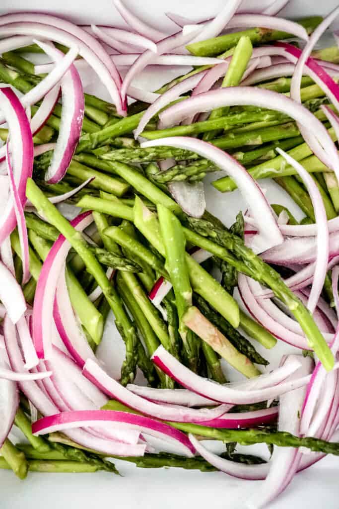 white baking dish with asparagus and red onion