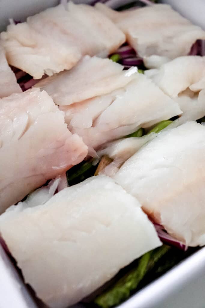 white baking dish with red onions and asparagus topped with haddock fillets