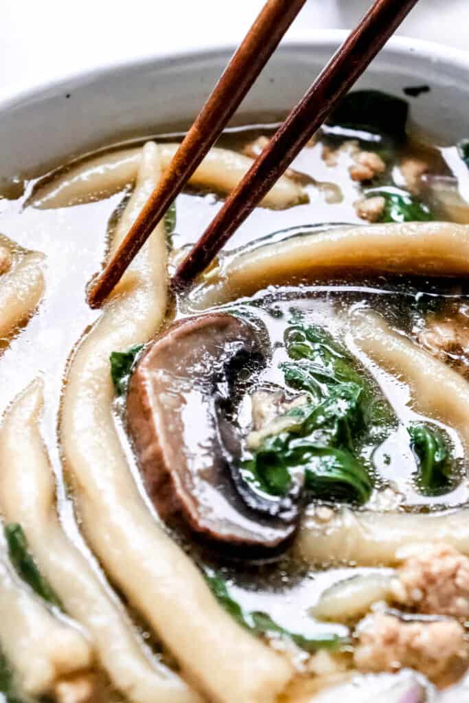 close up shot of soup with a pair of wooden chopsticks