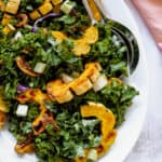 Large white platter with Roasted Delicata Squash and Kale Salad, two serving spoons and a pink cloth napkin