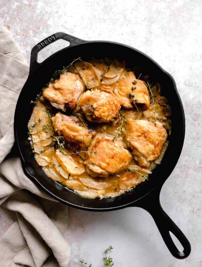 cast iron pan with chicken thighs, apples and fresh thyme with a brown cloth napkin