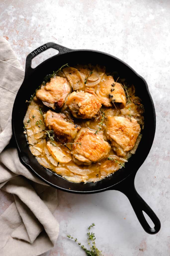 cast iron pan with chicken thighs, apples and fresh thyme with a brown cloth napkin