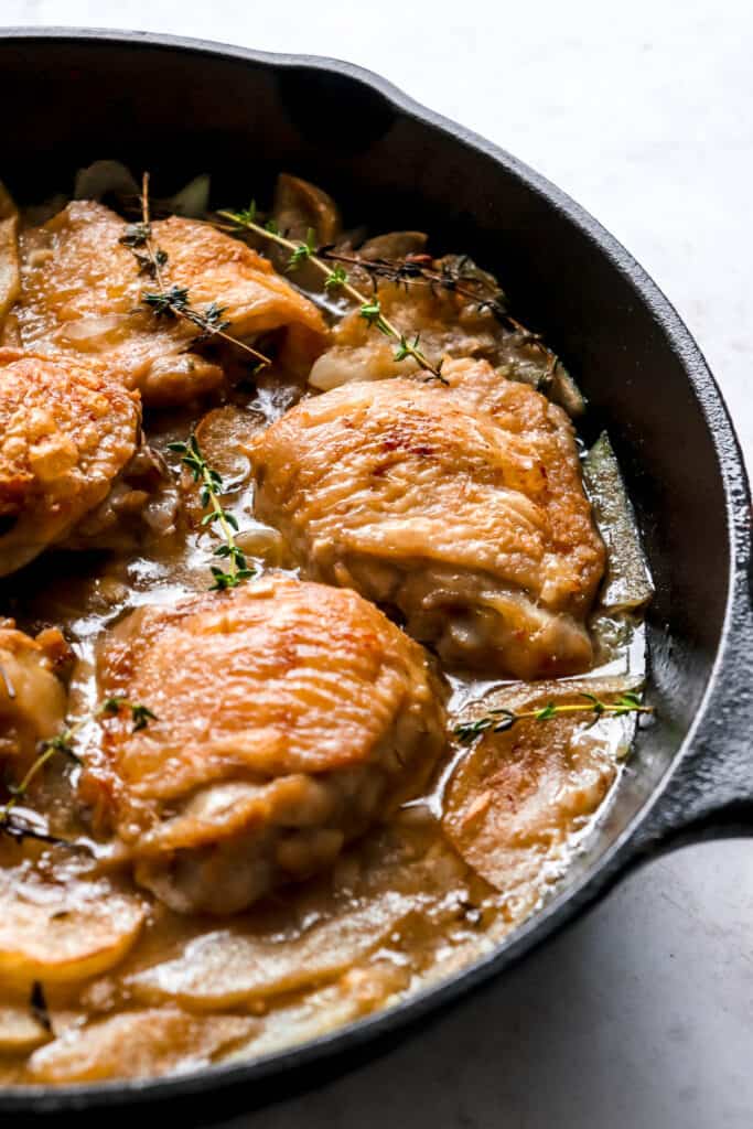 cast iron pan with chicken thighs, apples and fresh thyme