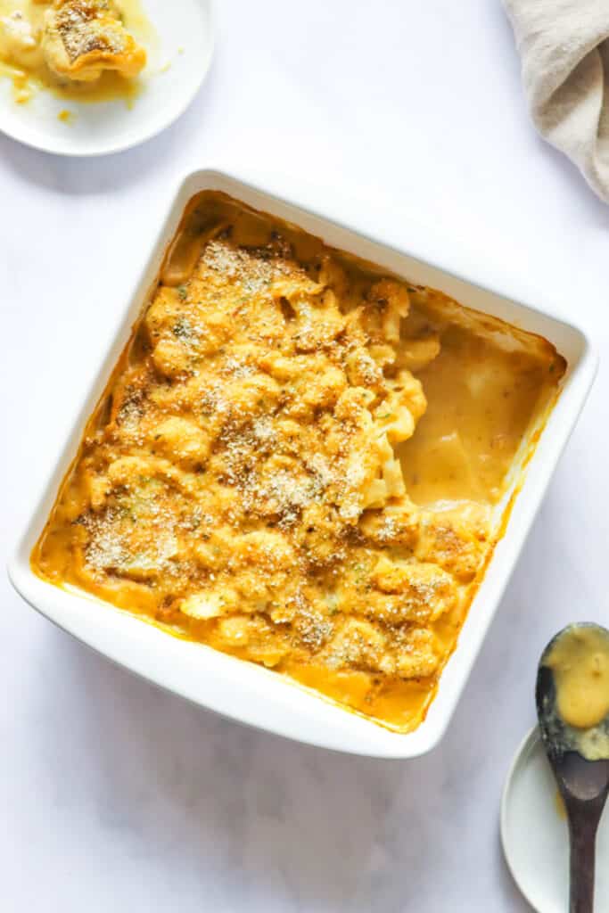 white baking dish with cauliflower gratin and herbed topping, side plate with a portion and a wooden baking spoon