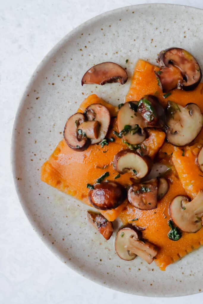 speckled plate with four sweet potato raviolis, topped with sliced mushrooms and spinach 