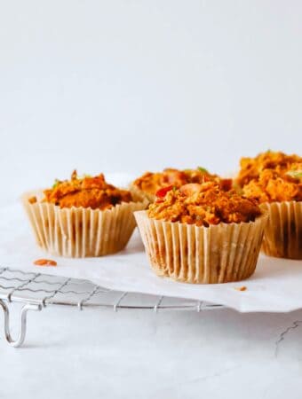 four sweet potato and bacon muffins in muffin liners on a white piece of parchment paper on top a round metal cooling rack