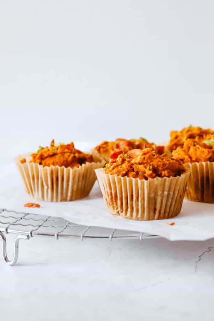 four sweet potato and bacon muffins in muffin liners on a white piece of parchment paper on top a round metal cooling rack