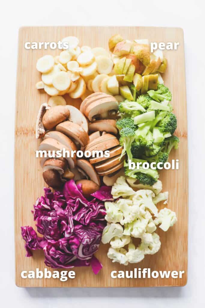 Wooden cutting board with chopped carrots, mushrooms, cabbage, cauliflower, broccoli and pears 