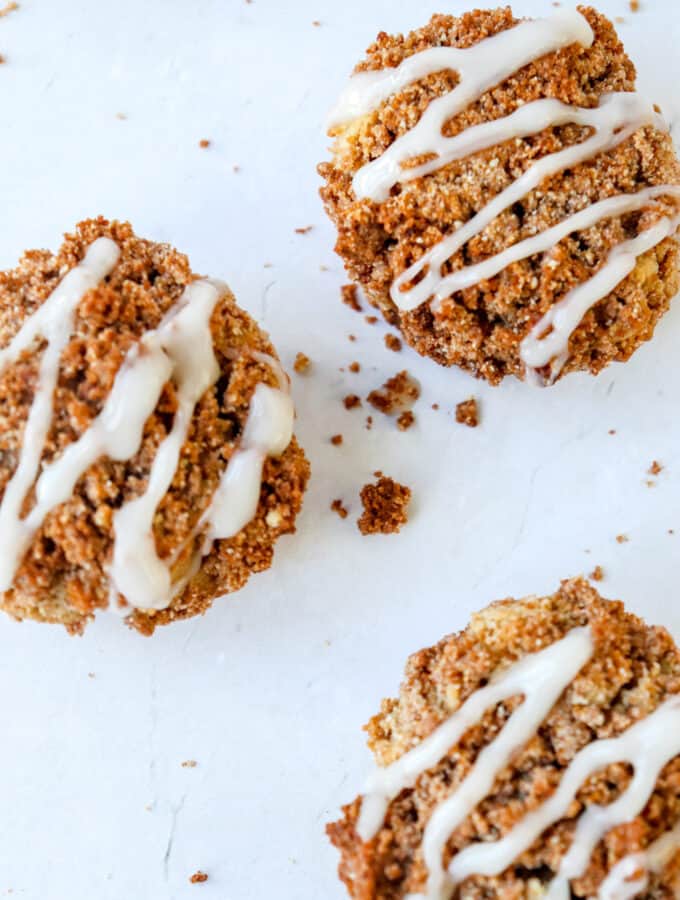 three cinnamon streusel muffins with coconut glaze drizzled on top