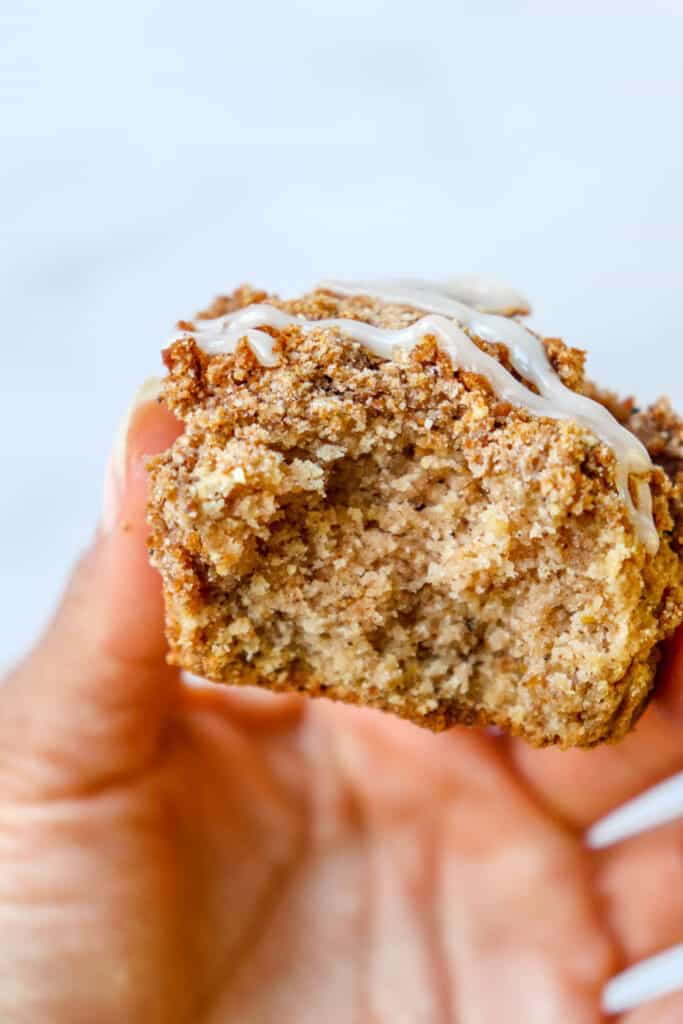 hand holding cinnamon streusel muffin with bite taken out of it