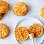 butternut squash biscuits on a light grey background with two white plates, one biscuit cut open with a honey drizzler