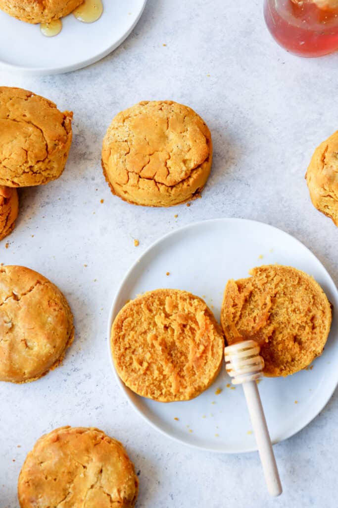 butternut squash biscuits on a light grey background with two white plates, one biscuit cut open with a honey drizzler