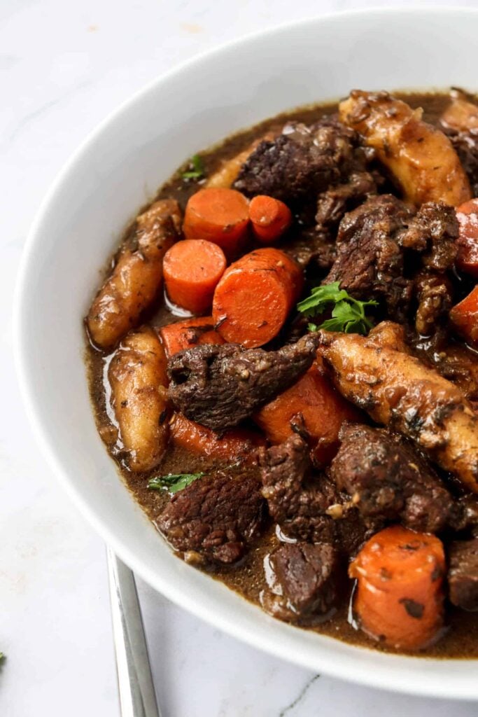 white bowl with stewed beef, carrots, cilantro and dumplings