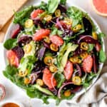 white platter with arugula, spinach, grapefruits, sliced beets and avocado, with wooden salad forks, a white bowl with salad dressing, a small bowl of salt, a bowl of kumquats, one half of a grapefruit and a package of spinach and arugula