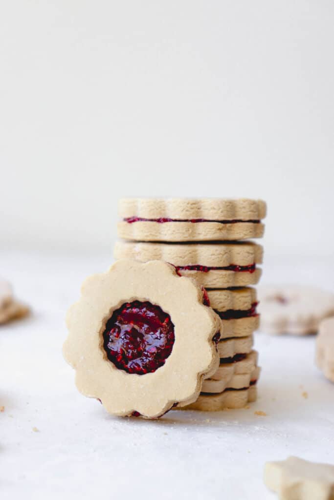 stack of linzer cookies against a white background with one cookie leaning against stack