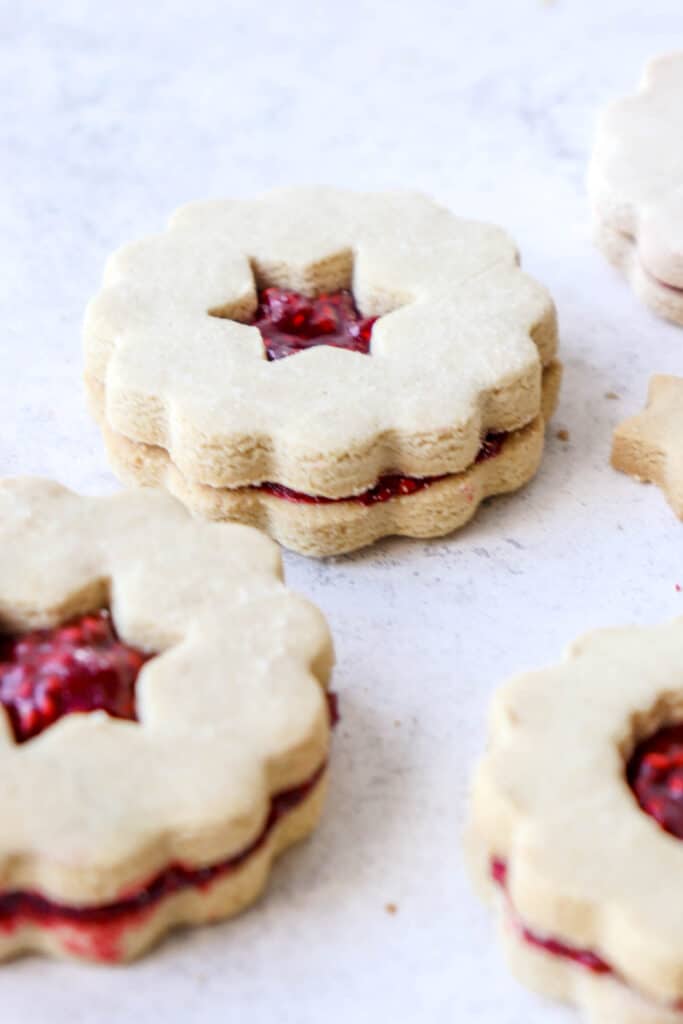 close up shot of raspberry filled linzer cookie with star cutout on a white backdrop with blurred linzer cookies in the foreground