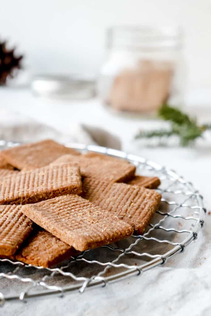 speculaas on a metal round cooling rack against a grey backdrop with a beige cloth napkin and a jar of cookies blurred in the background