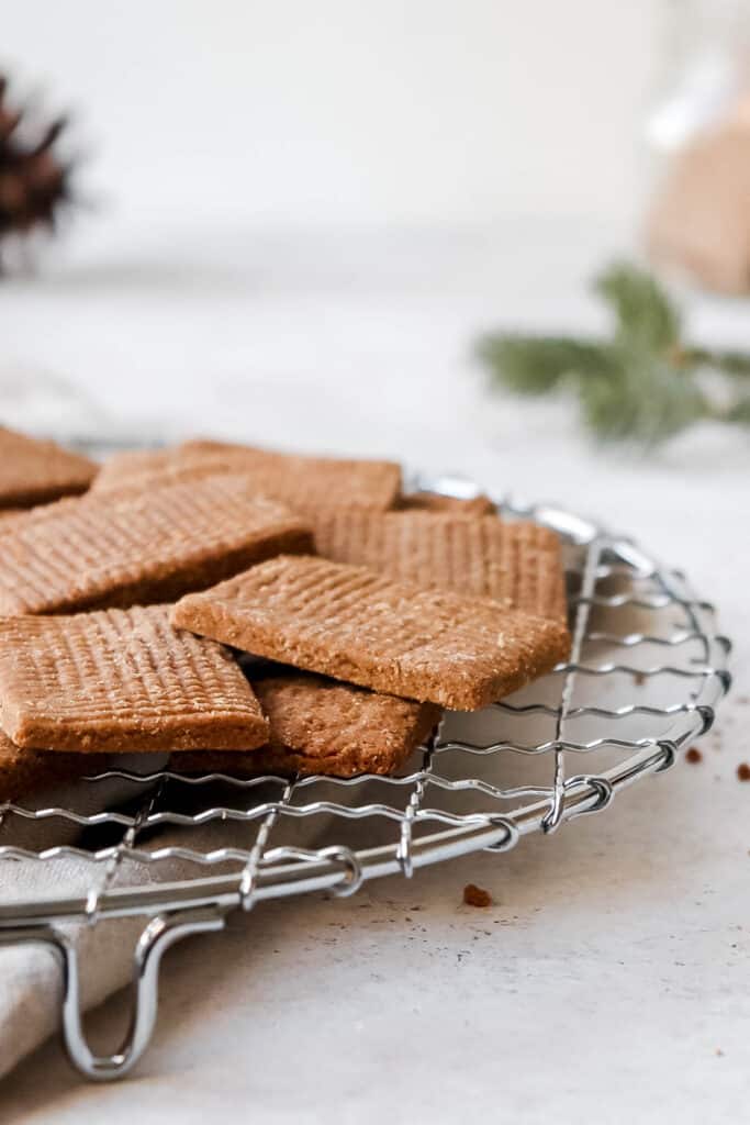 speculaas on a metal round cooling rack against a grey backdrop with a beige cloth napkin  and a jar of cookies blurred in the background