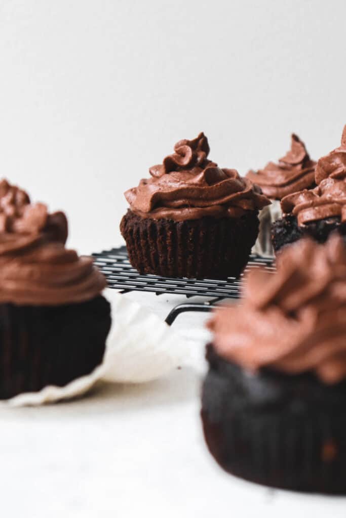 chocolate cupcakes with chocolate icing on a black cooling back with a few cupcakes in the foreground