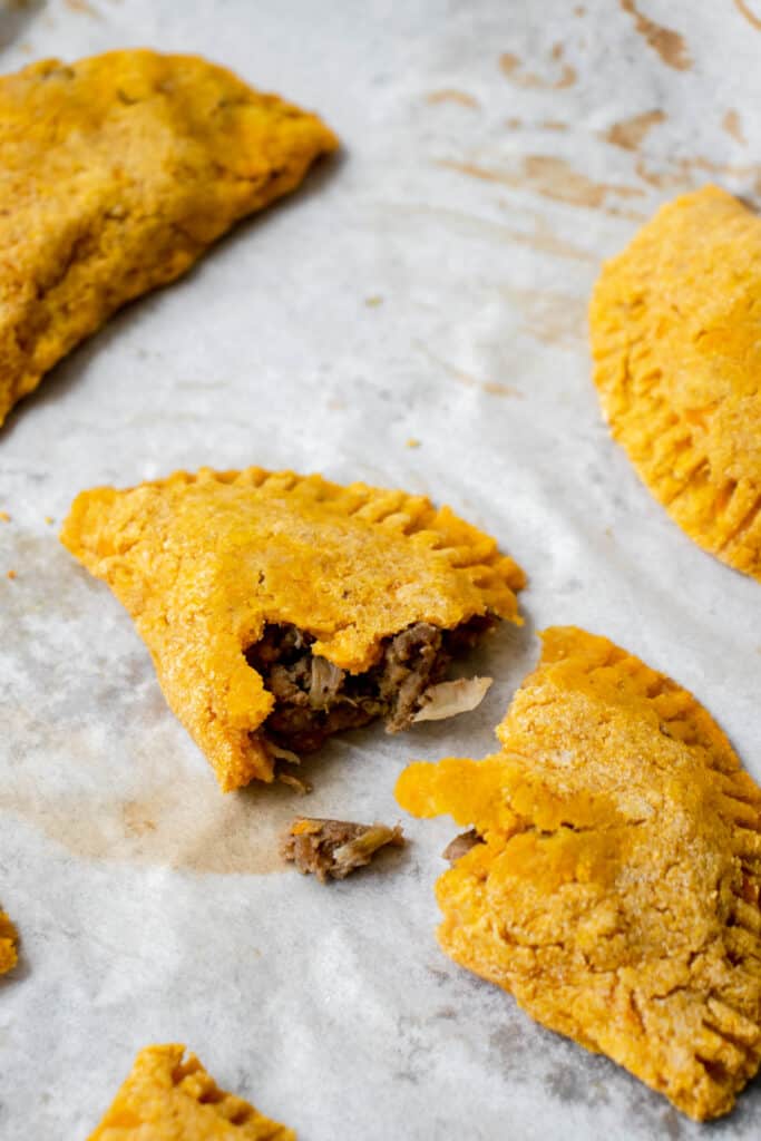 parchment paper with beef patties, with close up shot of one broken open exposing beef filling