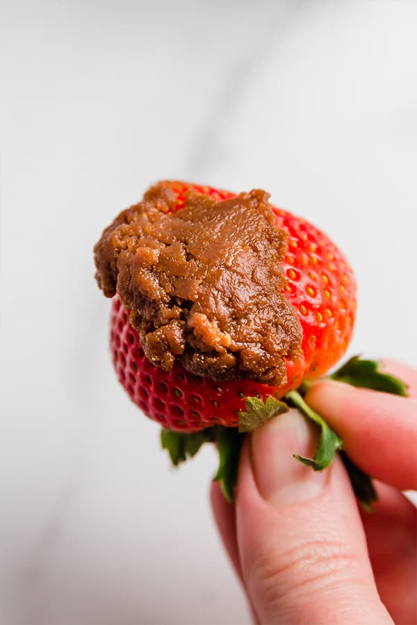 Hand holding strawberry smeared with cookie butter