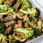 stainless steel sheet pan with beef, broccoli and mushrooms at an angle against a speckled grey background