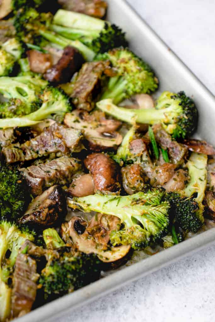 stainless steel sheet pan with beef, broccoli and mushrooms at an angle against a speckled grey background