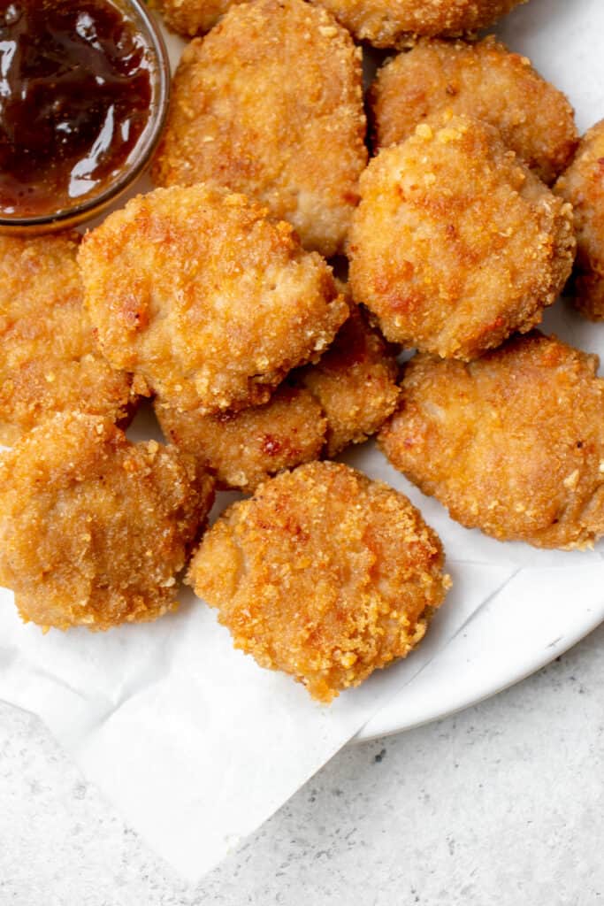 white plate with parchment paper topped with golden chicken nuggets and a glass bowl with brown sweet and sour dipping sauce