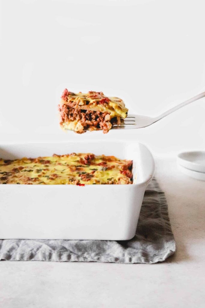 spatula lifting slice of lasagna up above a white dish of lasagna