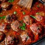 black cast iron skillet with lamb meatballs in nomato sauce with chopped parsley and a wooden spoon