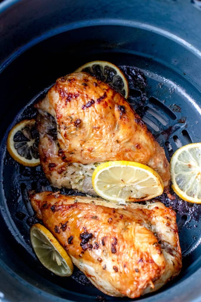 overhead shot of two chicken breasts in a grey air fryer basket with sliced lemons