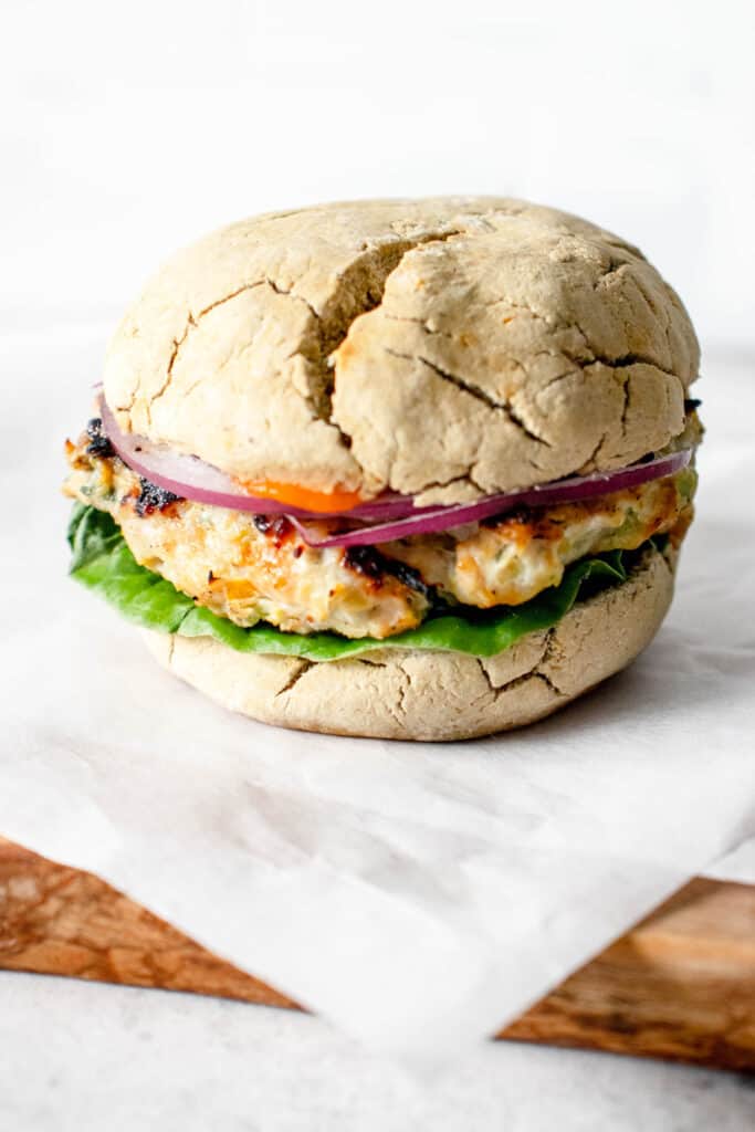 turkey burger between a sourdough biscuit with lettuce, onions and carrot ketchup on a white piece of parchment paper on a wooden block