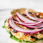 one turkey burger patty on one half of a sourdough biscuit with lettuce and sliced red onion on a white plate