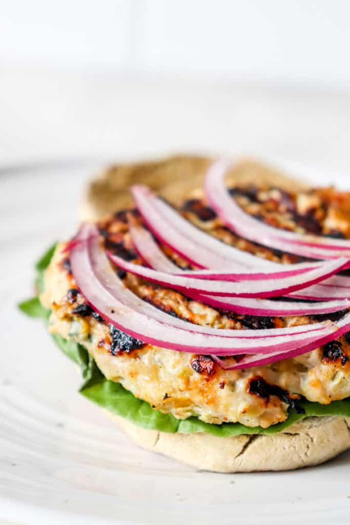 one turkey burger patty on one half of a sourdough biscuit with lettuce and sliced red onion on a white plate